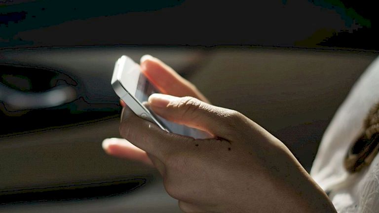 A person using a smartphone while sitting in a car, with a part of the interior and their clothing visible.