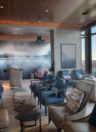 A modern lounge with comfortable seating, large windows offering views of a cityscape and water, and a wall mural featuring a skyline completes the picture.