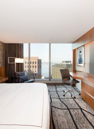 A modern hotel room with a large bed, desk, chair, and flat-screen TV, featuring a city view through a large window, ends the sentence.
