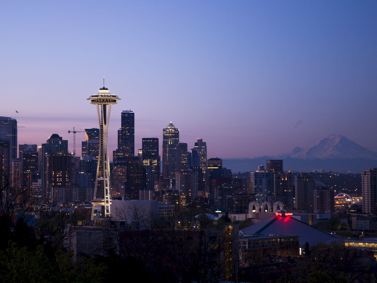 A scenic view of Seattle's skyline at dusk, featuring the Space Needle and Mount Rainier in the background under a twilight sky ending the sentence.